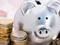 Hucha plateada rodeada de pilas de monedas de euro, simbolizando las ventajas del euro para el ahorro.