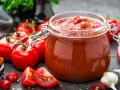 Słoik pełen domowego przecieru pomidorowego, otoczony świeżymi pomidorami, papryczkami chili i czosnkiem. Idealny do sosów i zup.