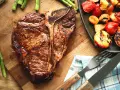 Un succulent côte de bœuf grillé, accompagné d'asperges et de tomates rôties, prêt à être dégusté.