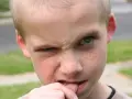 Chłopiec, który ma 3 latek, obgryza paznokcie. Jego twarz jest pełna piegów, a oczy wyrażają skupienie.