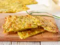 Schiacciata di zucchine dorata e croccante, con erbe aromatiche, servita su un tagliere di legno.
