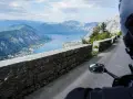 Widok z motocykla na Zatokę Kotorską w Czarnogórze. Kręta droga z kamiennym murem i zapierająca dech w piersiach panorama gór i morza.