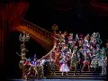 Tłum w barwnych maskach i kostiumach na schodach opery. To scena z musicalu, gdzie magia i tajemnica splatają się w widowiskowym spektaklu.