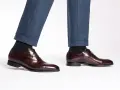 Eleganza senza tempo: un uomo indossa pantaloni blu e scarpe oxford non brogue marroni lucide, perfette per ogni occasione formale.