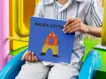 Chłopiec trzyma książkę "Nauka czytania dla 6 latka" z zabawną literką "A" na okładce.