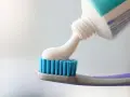 Biała pasta do zębów wylewa się z tubki na niebieskie włosie szczoteczki.