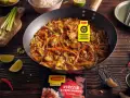 Kurczak w pięciu smakach po chińsku w woku, z warzywami i ryżem w tle. Obok limonki, chili i czosnek.
