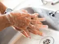 Manos con jabón bajo un chorro de agua en un lavabo.