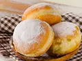 Trzy puszyste pączki, dwa posypane cukrem pudrem, leżą na drewnianej misce. Idealne na tłusty czwartek, te fit pączki kuszą apetycznym wyglądem.