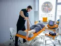Fizjoterapeuta wykonuje zabieg naświetlania kręgosłupa pacjentowi leżącemu na kozetce.
