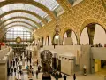 Interior del museo d'Orsay, con su impresionante techo de cristal y arcos dorados. Visitantes pasean entre esculturas y obras de arte.