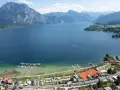 Idyllischer **Camping Traunsee** mit Blick auf den See und die Berge. Boote liegen im Hafen, Tennisplätze und Wohnwagen sind zu sehen.