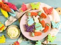 Bunte Osterkekse in Hasen-, Karotten- und Schmetterlingsform, bereit für ein einfaches Osterkekse Rezept. Spritzbeutel mit Zuckerguss liegen bereit.