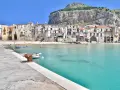 Coastal town with buildings nestled against a cliff, turquoise water, and boats. Perfect for a 10 days in Sicily adventure.