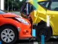 Zderzenie dwóch samochodów, pomarańczowego i żółtego. Dowiedz się, jak zgłosić szkodę auta po wypadku.