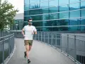 Uomo con barba corre su un ponte moderno, mostrando cos'è il running: libertà e benessere tra architettura e natura.