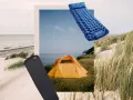 Zwei Isomatten, eine blaue aufblasbare und eine schwarze Schaumstoffmatte, liegen neben einem orangefarbenen Zelt am Strand.