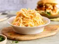 Schüssel mit cremigem Krautsalat, perfekt für ein **Rezept Coleslaw original**. Im Hintergrund ein Burger.