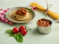 Pyszny sos do spaghetti z mięsem mielonym, podany na talerzu z makaronem, obok świeżych pomidorków i bazylii.