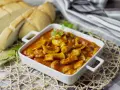 Delicioso plato de sepia en salsa, servido en cazuela blanca, acompañado de pan rústico y hojas de laurel.