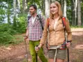 Ein Paar wandert achtsam durch einen Wald. Die Frau und der Mann nutzen Wanderstöcke, eine Anleitung für einen achtsamkeitsspaziergang.
