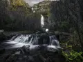 Cascada en el **río Bornova**, con aguas sedosas cayendo entre rocas y vegetación otoñal, bajo un cielo nublado.