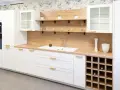 Cocina moderna blanca con encimera de madera, estantes flotantes y botellero. Inspiración para tus ideas de cocinas.
