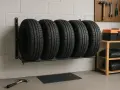 Cinque pneumatici da auto sono disposti su un supporto a muro. Sullo scaffale a destra, una cassetta degli attrezzi arancione e nera e due sacchi neri.