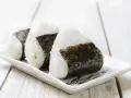 Trzy ryżowe kulki onigiri z nori na białym talerzyku. Idealne na szybki lunch, oto prosty onigiri przepis.
