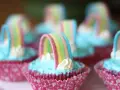 Sju cupcakes med ljusblå regnbågs frosting och godisregnbågar. Rosa muffinsformar med mönster.