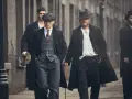 Tommy Shelby e altri uomini in abiti eleganti camminano per strada.