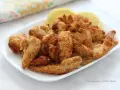 Straccetti di pollo in friggitrice ad aria, dorati e croccanti, serviti su un piatto bianco con spicchi di limone.