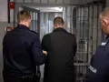 Dwóch policjantów eskortuje mężczyznę do celi. Może to być związane z zabezpieczeniem majątkowym.