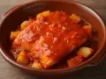 Bacalao a la riojana, un plato tradicional con trozos de patata y pimiento en una salsa roja sabrosa, servido en cazuela de barro.