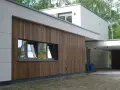 Nowoczesny dom z białymi panelami i elewacjami drewnianymi pionowymi. Okna odbijają drzewa.