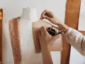 Mani che lavorano su un manichino, creando un modello di cartone. Un corso di modellistica in pieno svolgimento, con pizzi e accessori da cucito a portata di mano.