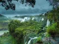 Majestuosas cataratas del Iguazú, un torrente de agua cayendo entre exuberante vegetación bajo un cielo nublado.