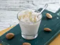 Rinfrescante granita alla mandorla, guarnita con lamelle di mandorle, servita in un bicchiere su un tagliere scuro.
