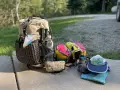 Backpack, water bottle, hiking poles, and colorful pouches are laid out, ready for a trip. This is how to pack light for an adventure.