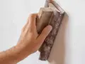 Mano lijando una pared con lija para pared y bloque de madera.