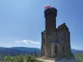 Kamienna wieża z polską flagą, część zamku księcia Henryka, góruje nad malowniczym krajobrazem gór i lasów.