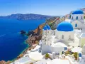 Santorini wycieczki: białe domy z niebieskimi kopułami na klifie nad błękitnym morzem. Statek płynie w oddali.