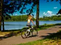 Kobieta na rowerze przemierza malownicze **trasy rowerowe Mazury** wzdłuż jeziora.