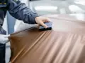 Applying a bronze vinyl wrap to a car hood, showing the process of how to wrap a truck for a custom look.