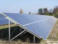Duża instalacja PV na polu, panele słoneczne ustawione pod kątem, w tle drzewa i błękitne niebo.