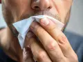 Mężczyzna wyciera nos chusteczką. Czy to przeziębienie, czy może alergia? Ten **slinotok od czego** może być uciążliwy.
