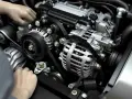 Hände am Motor, die Lichtmaschine ist sichtbar. Mögliche lichtmaschine defekt symptome sind hier zu sehen, wie ein lockerer Keilriemen.