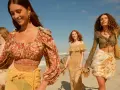Quattro donne con abiti in stile boho passeggiano su una spiaggia sabbiosa con il mare sullo sfondo.