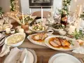 Mesa de Nochevieja con carnes asadas, ensaladas, velas y luces festivas.