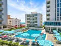 Albania - wczasy samolotem all inclusive. Basen hotelowy z leżakami i parasolami, w tle budynki i morze. Idealne miejsce na relaks.